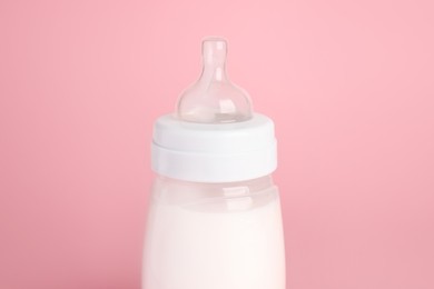 Photo of One feeding bottle with milk on pink background, closeup