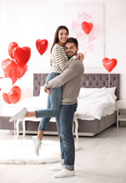 Photo of Lovely young couple in bedroom decorated with heart shaped balloons. Valentine's day celebration