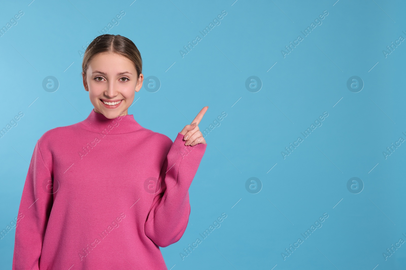 Photo of Beautiful teenage girl pointing at something on light blue background. Space for text