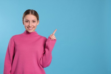 Photo of Beautiful teenage girl pointing at something on light blue background. Space for text