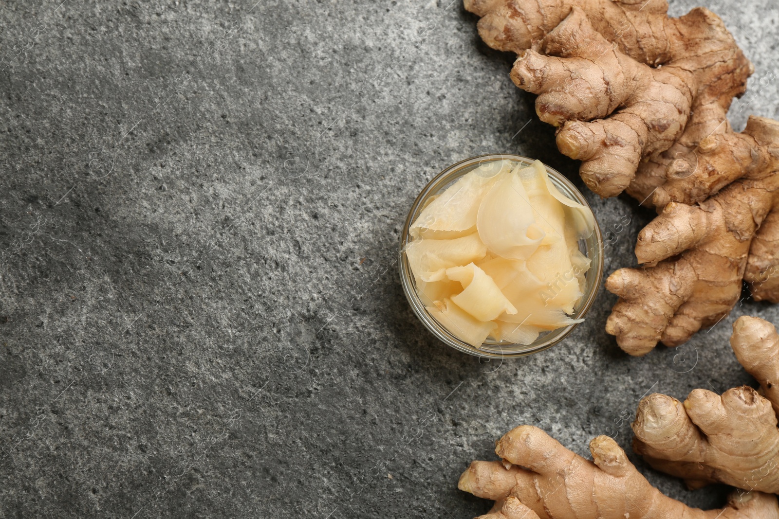 Photo of Spicy pickled ginger and root on grey table, flat lay. Space for text