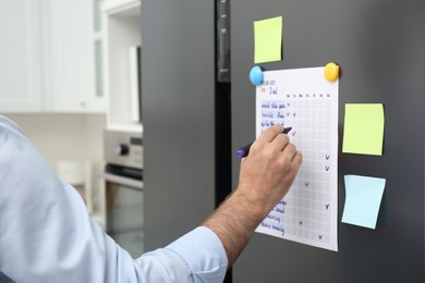 Photo of Man checking to do list on fridge in kitchen, closeup