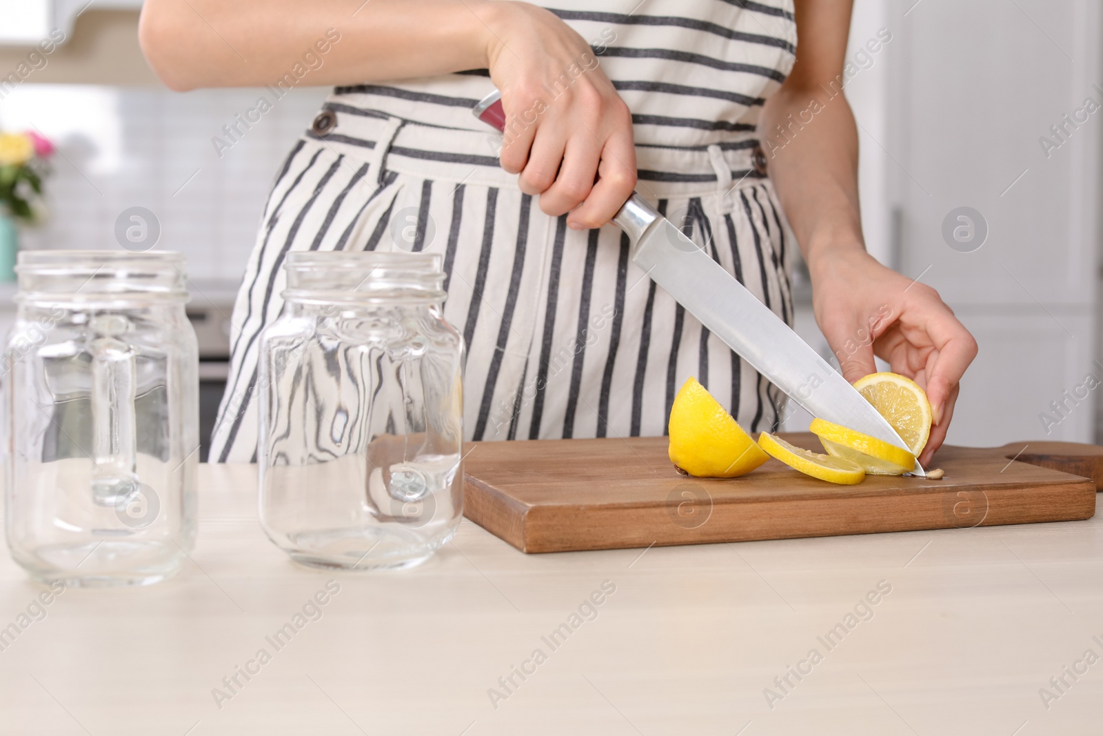 Photo of Young woman preparing lemonade on table, closeup. Natural detox drink