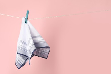 Handkerchief hanging on rope against pink background, space for text