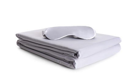 Photo of Stack of clean silky bed linen and sleeping mask isolated on white