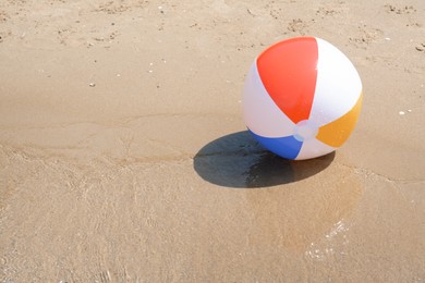 Colorful beach ball on wet sand at seaside, space for text