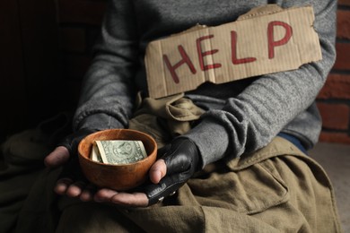 Poor homeless man with help sign holding bowl of donations, closeup