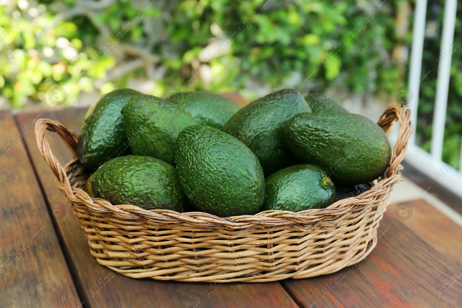 Photo of Wicker basket with fresh ripe avocados on wooden table outdoors