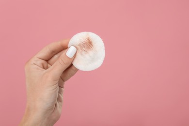 Photo of Woman with dirty cotton pad after removing makeup on pink background, closeup. Space for text