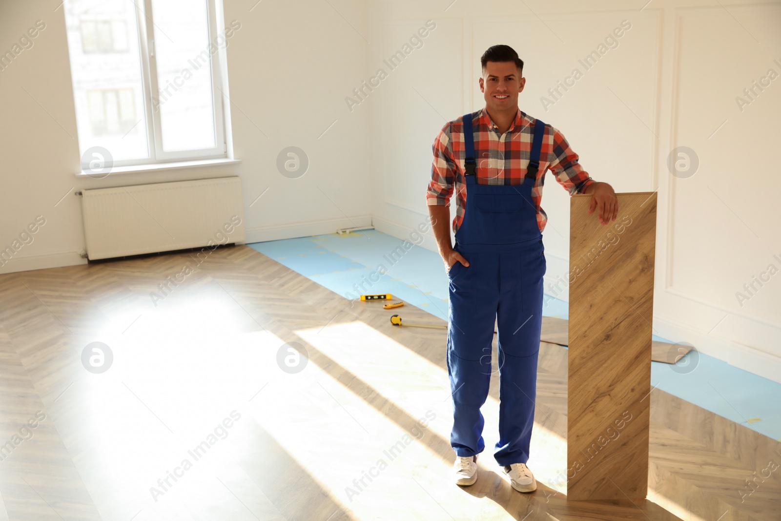 Photo of Professional worker with wooden board indoors. Installing of parquet flooring