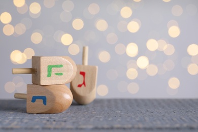 Hanukkah traditional dreidels with letters Nun, He and Gimel on grey wooden table against blurred lights. Space for text