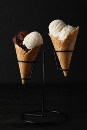 Photo of Ice cream scoops in wafer cones on black wooden table against dark background