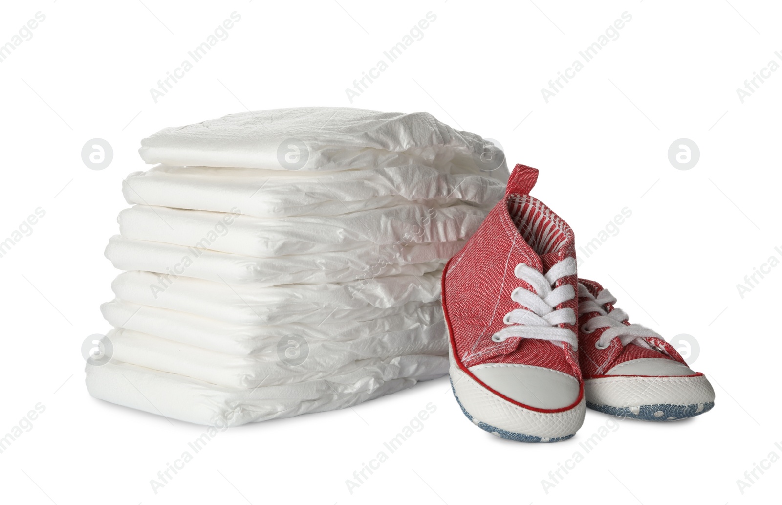 Photo of Stack of disposable diapers and child's shoes on white background