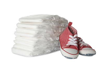 Photo of Stack of disposable diapers and child's shoes on white background