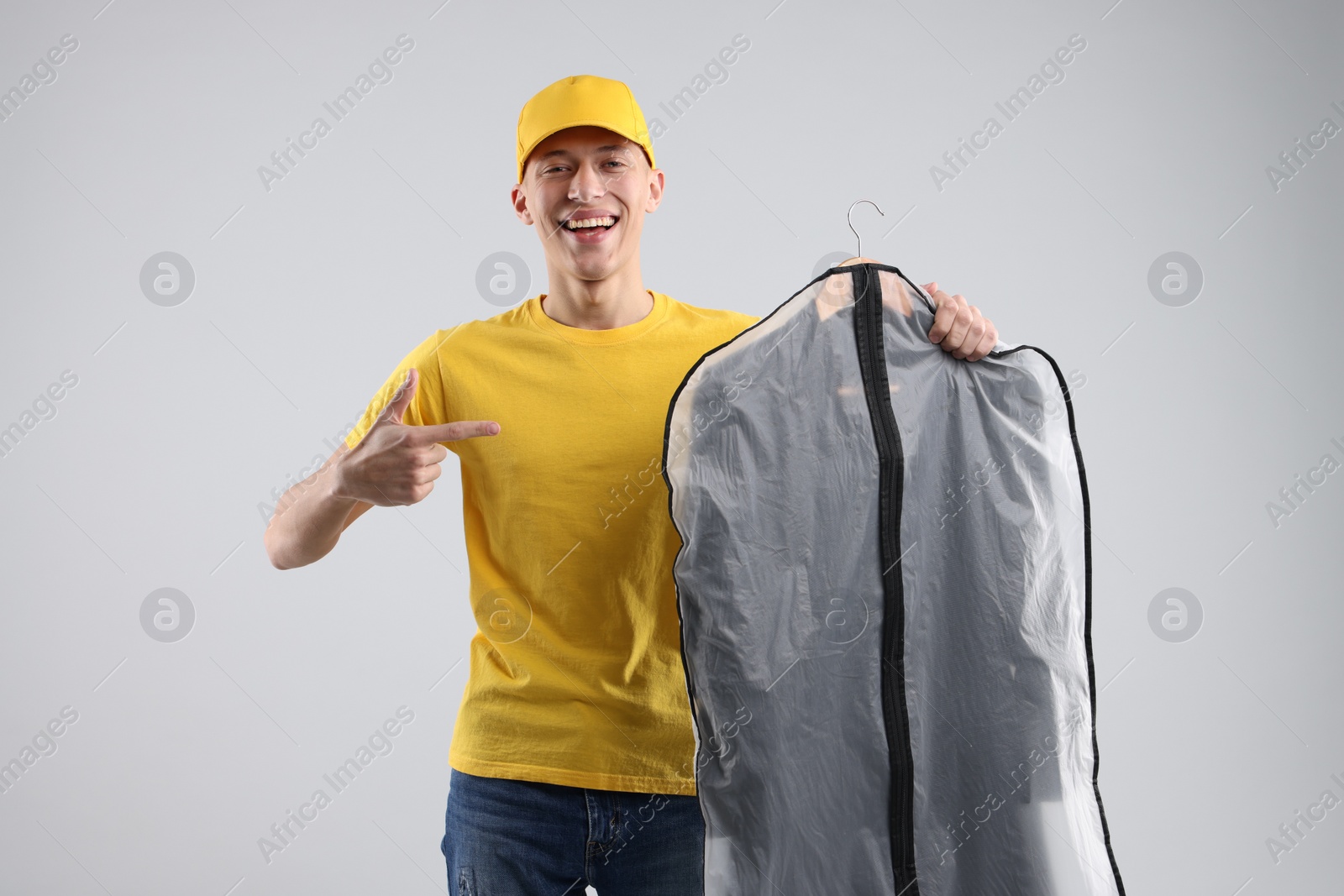 Photo of Dry-cleaning delivery. Happy courier holding garment cover with clothes on light grey background