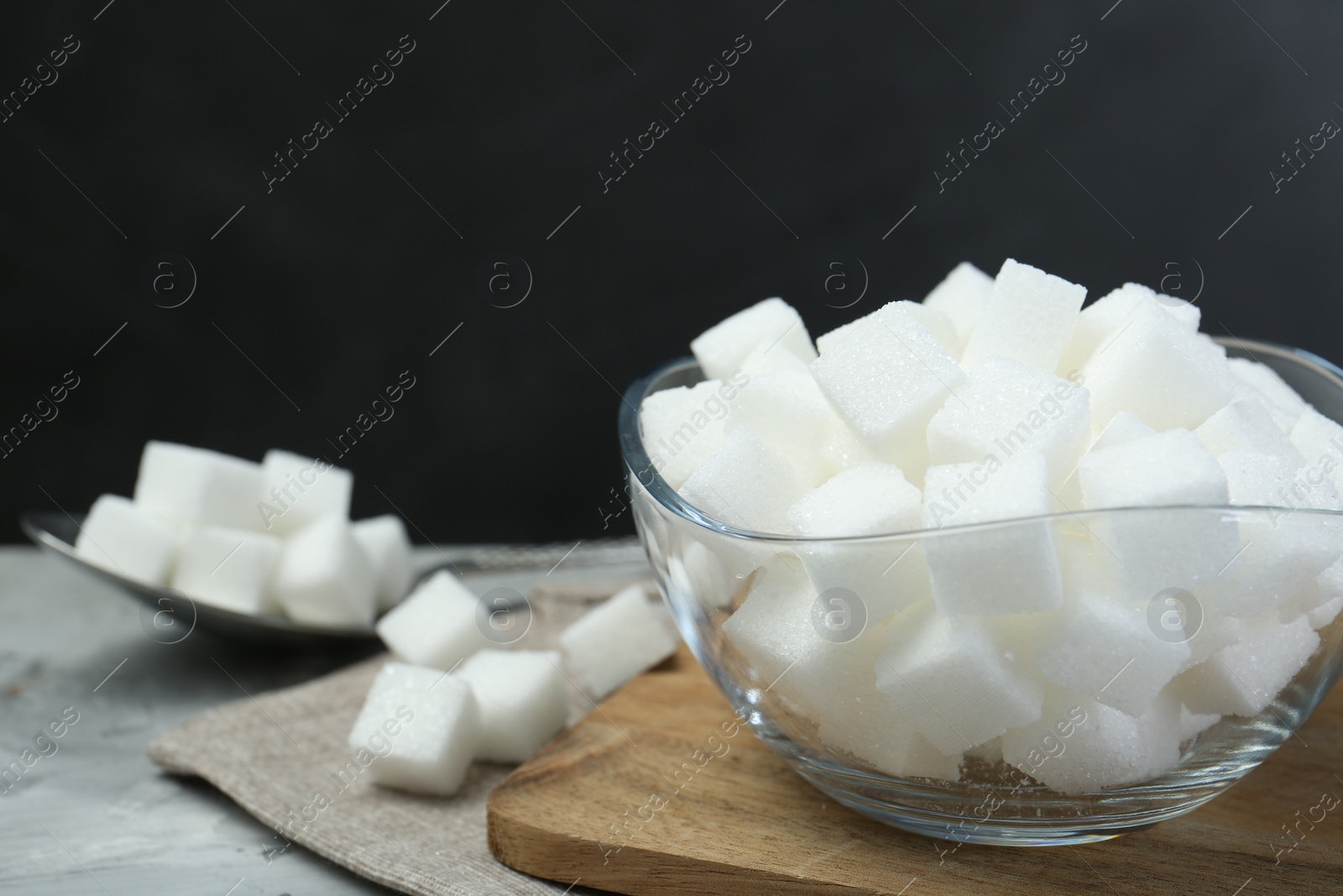 Photo of White sugar cubes in glass bowl on grey table, space for text