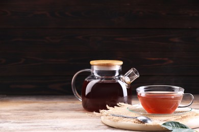 Photo of Aromatic hot tea in glass cup and teapot on wooden table. Space for text
