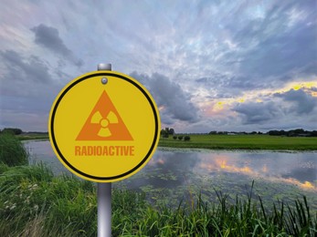 Image of Radioactive pollution. Yellow warning sign with hazard symbol near lake