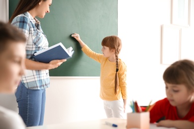 Young teacher and girl near chalkboard in classroom