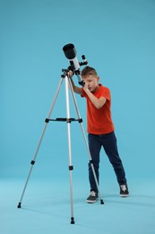 Little boy looking at stars through telescope on light blue background