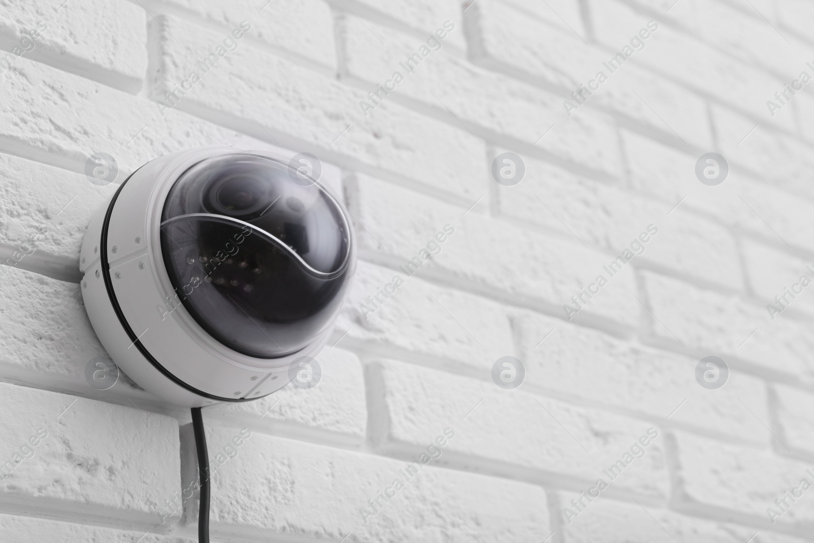 Photo of Modern CCTV security camera on white brick wall. Space for text