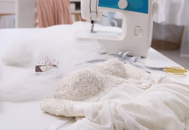 Photo of Beautiful wedding dress with embroidered bustline on table in dressmaking workshop
