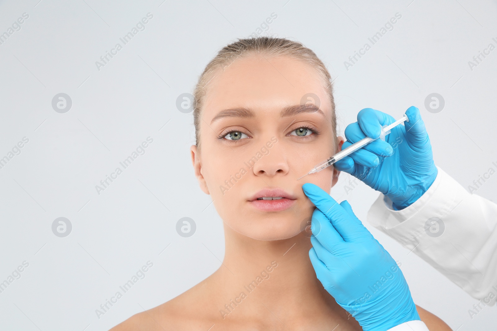 Photo of Young woman getting facial injection on white background. Cosmetic surgery concept