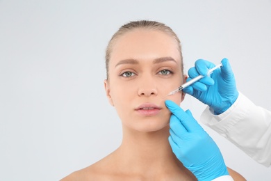 Young woman getting facial injection on white background. Cosmetic surgery concept