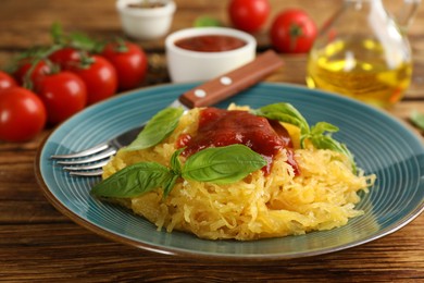 Photo of Tasty spaghetti squash with tomato sauce and basil served on wooden table, closeup