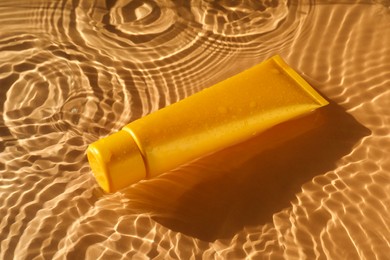 Photo of Tube with moisturizing cream in water on orange background