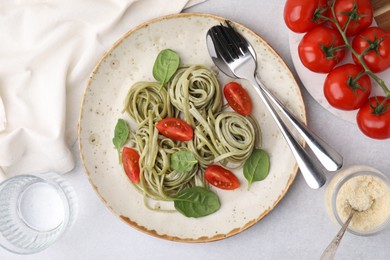 Photo of Tasty pasta with spinach and tomatoes served on light grey table, flat lay