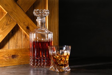 Photo of Whiskey with ice cubes in glass and bottle on grey table, space for text