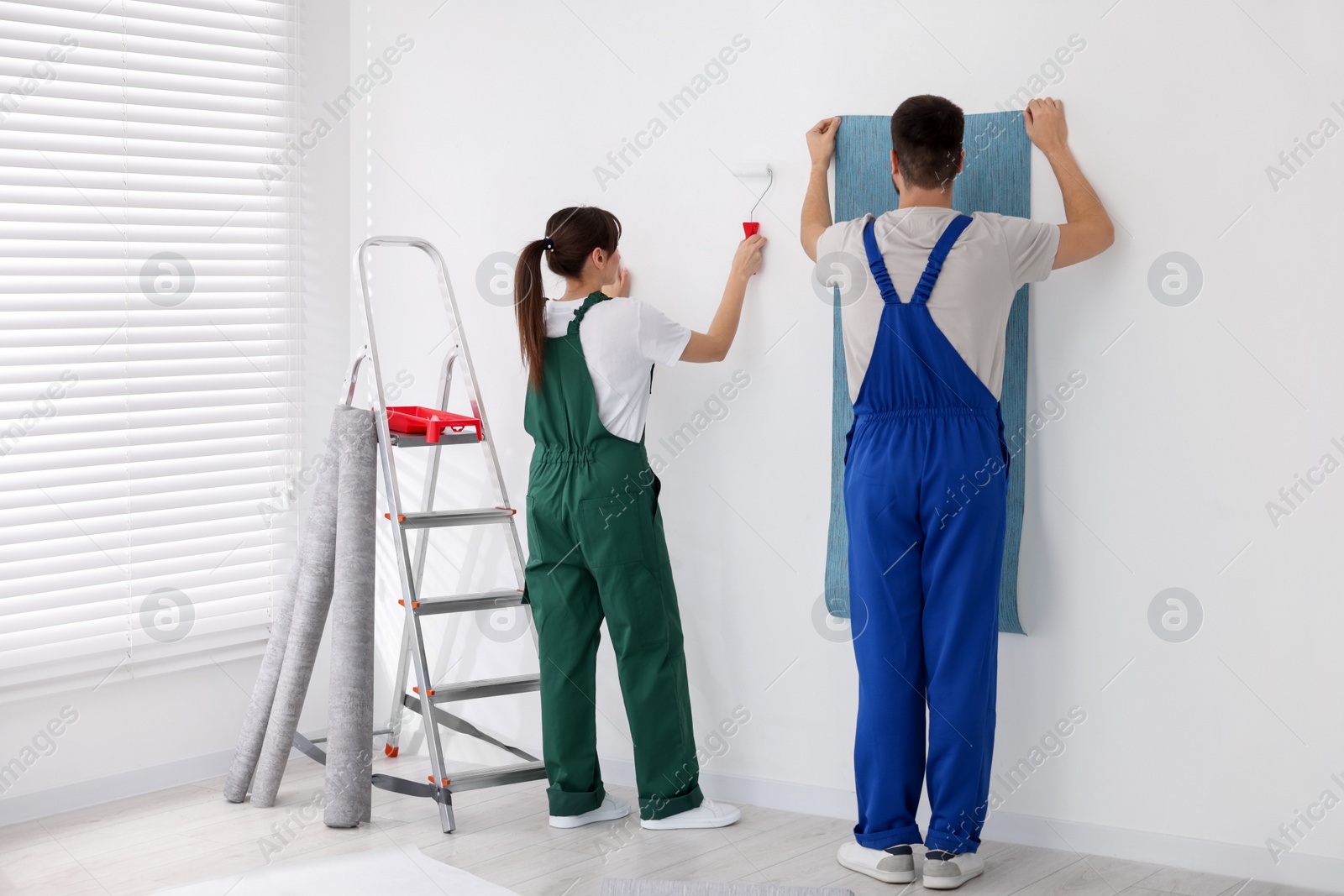 Photo of Workers hanging light blue wallpaper in room