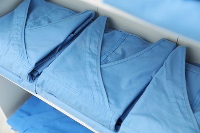 Light blue medical uniforms on white rack, closeup