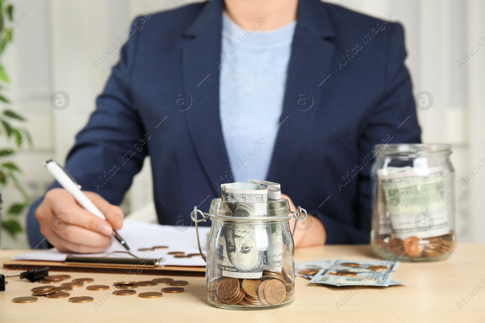 Photo of Woman with glass jar of money at wooden table, closeup