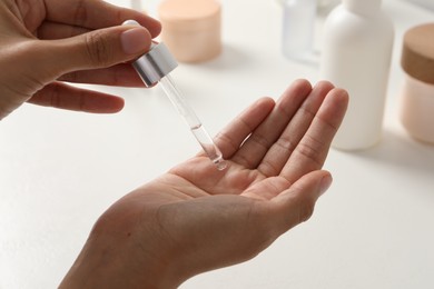 Photo of Woman applying cosmetic serum onto her hand at white table, closeup