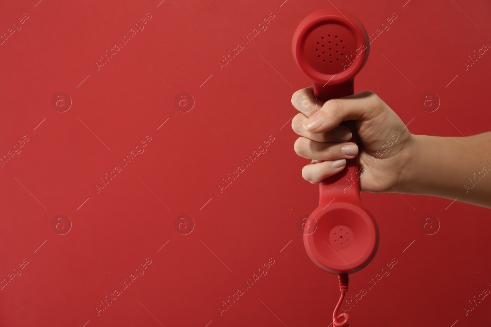 Photo of Closeup view of woman holding corded telephone handset on red background, space for text. Hotline concept