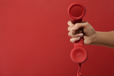 Closeup view of woman holding corded telephone handset on red background, space for text. Hotline concept