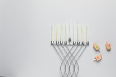Photo of Hanukkah menorah with candles and dreidel on light background, flat lay. Space for text