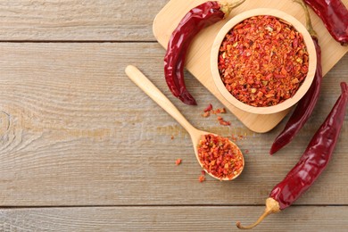 Photo of Aromatic spice. Red chili pepper flakes in bowl, spoon and pods on wooden table, flat lay. Space for text