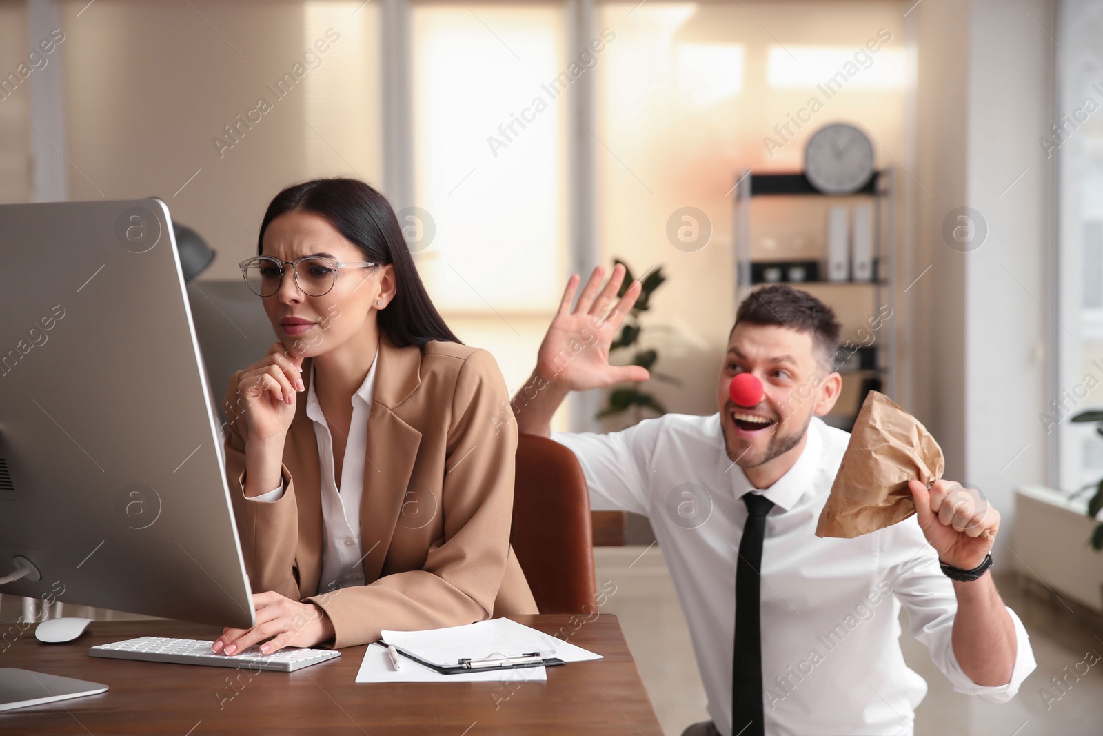 Photo of Man popping paper bag behind his colleague in office. Funny joke