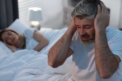 Photo of Irritated man covering his ears in bed at home, space for text. Problem with snoring wife