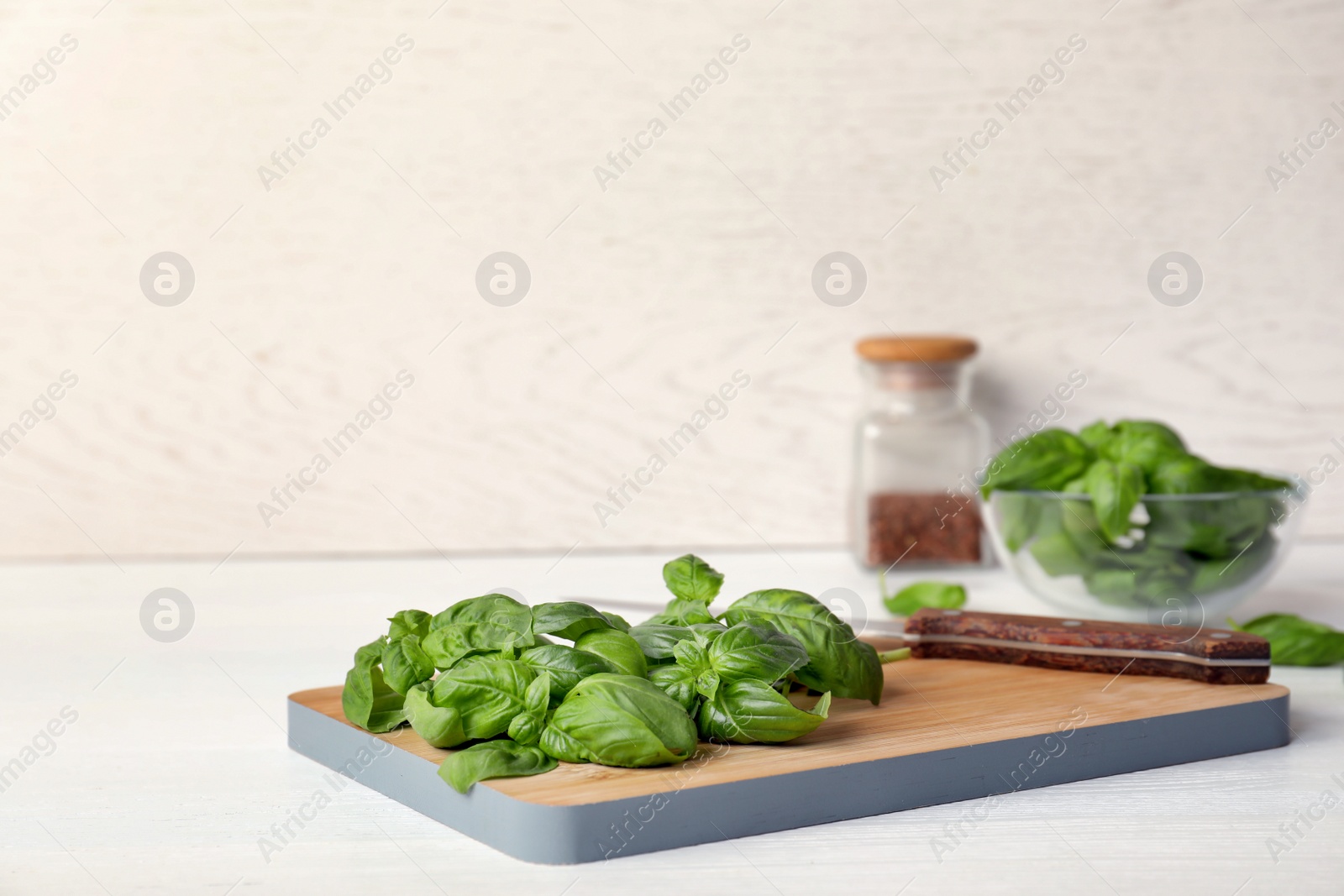 Photo of Wooden board with fresh green basil leaves on table. Space for text