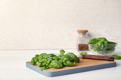 Photo of Wooden board with fresh green basil leaves on table. Space for text