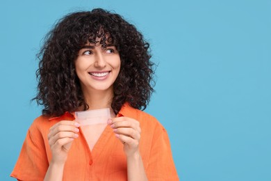 Young woman holding teeth whitening strips on light blue background, space for text