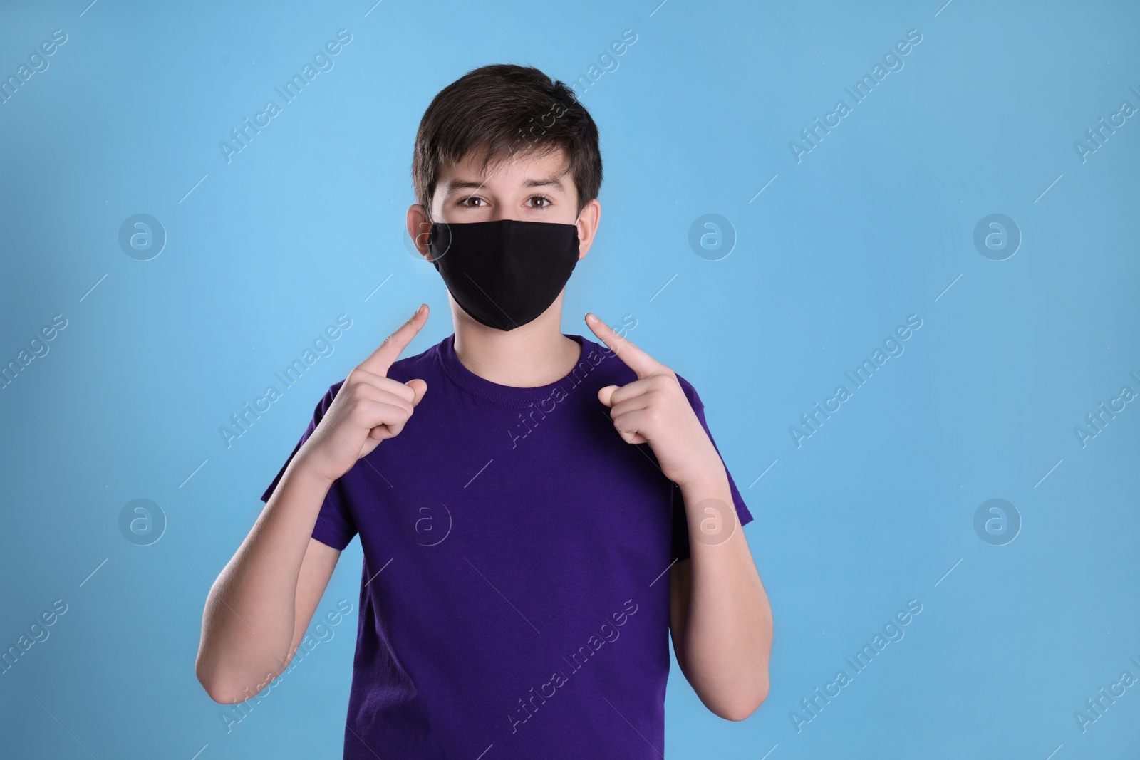 Photo of Boy wearing protective mask on light blue background. Child safety