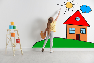 Image of Cute child drawing landscape with house on white wall indoors