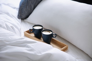 Photo of Wooden tray with cups of coffee near soft blanket on bed