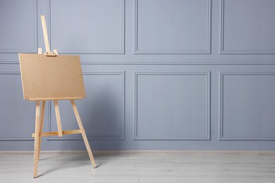 Photo of Wooden easel with blank board near grey wall indoors. Space for text