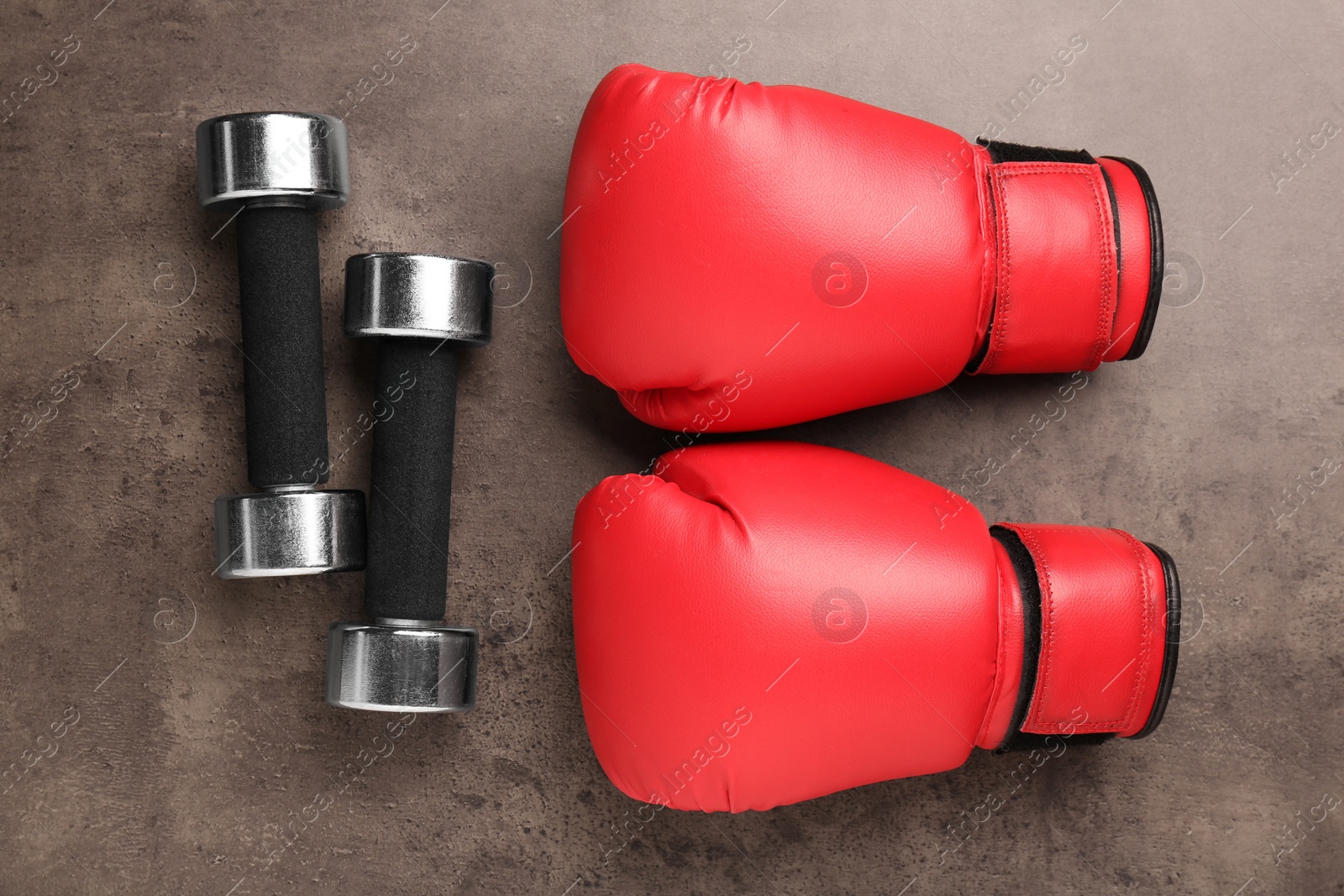 Photo of Metal dumbbells and boxing gloves on brown textured table, flat lay